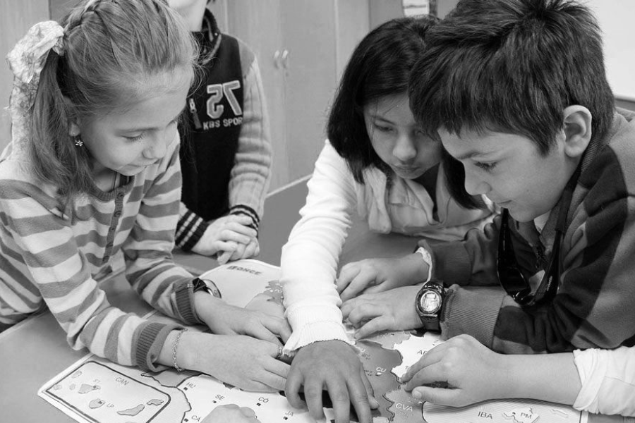 Foto en blanco y negro de niños en un entorno escolar mirando y señalando un mapa.